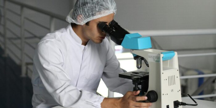 Scientist in a lab coat using a microscope to conduct research, focusing on healthcare improvements.