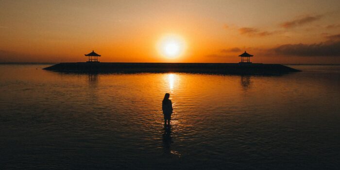 A tranquil scene of a silhouette at sunrise near pavilions on a Bali beach.